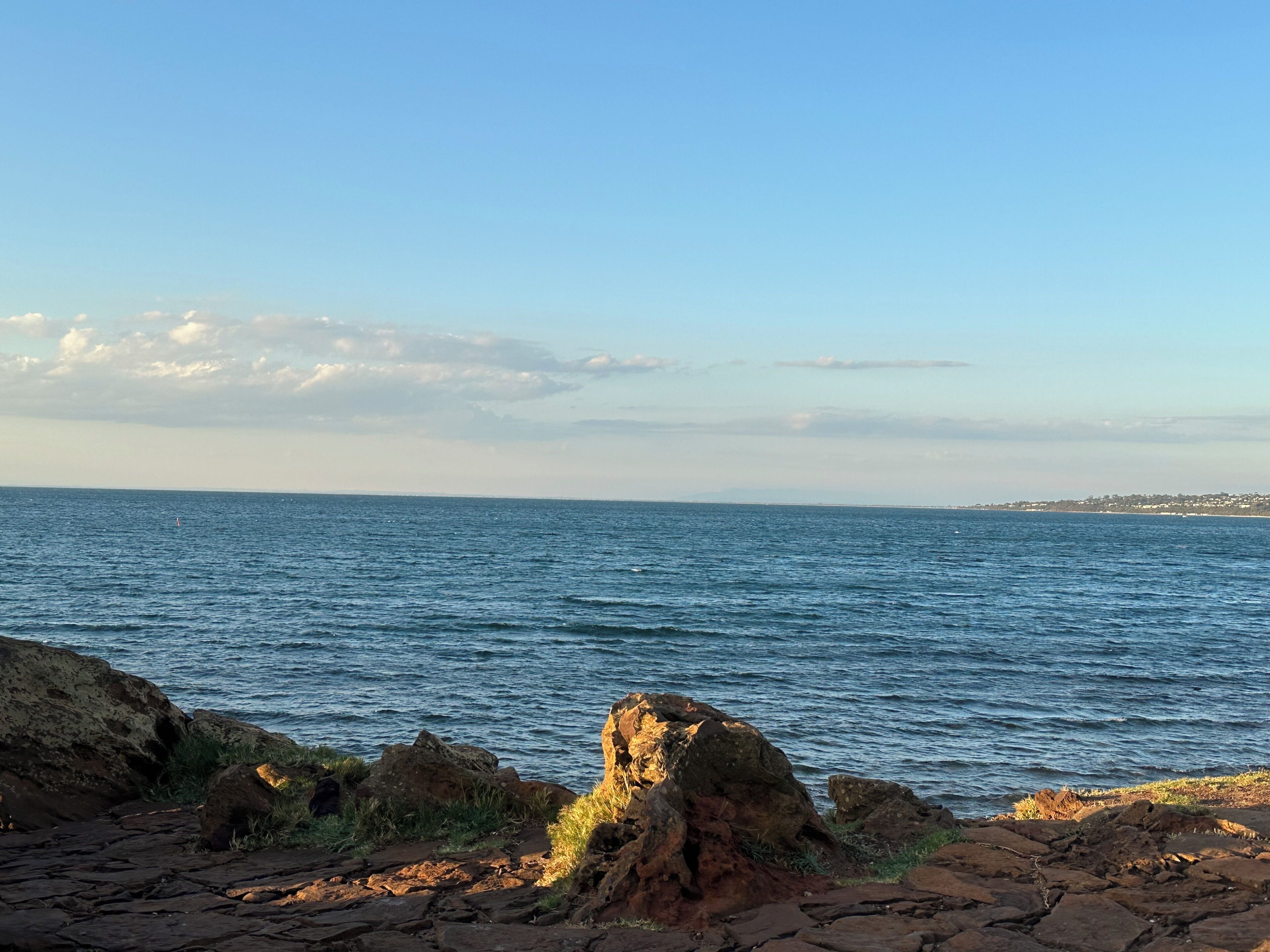 Paesaggio costiero con uno sfondo roccioso e mare calmo.