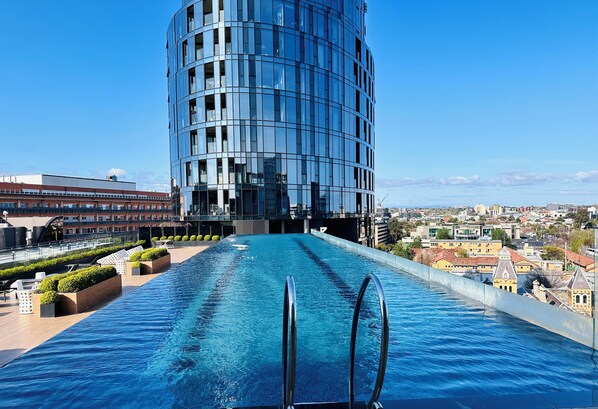 Une piscine à débordement située sur le toit, offrant une vue sur un bâtiment moderne et le paysage urbain.