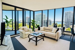 Un salon moderne comprenant un canapé, des fauteuils, une table basse et de grandes fenêtres donnant sur la ville.