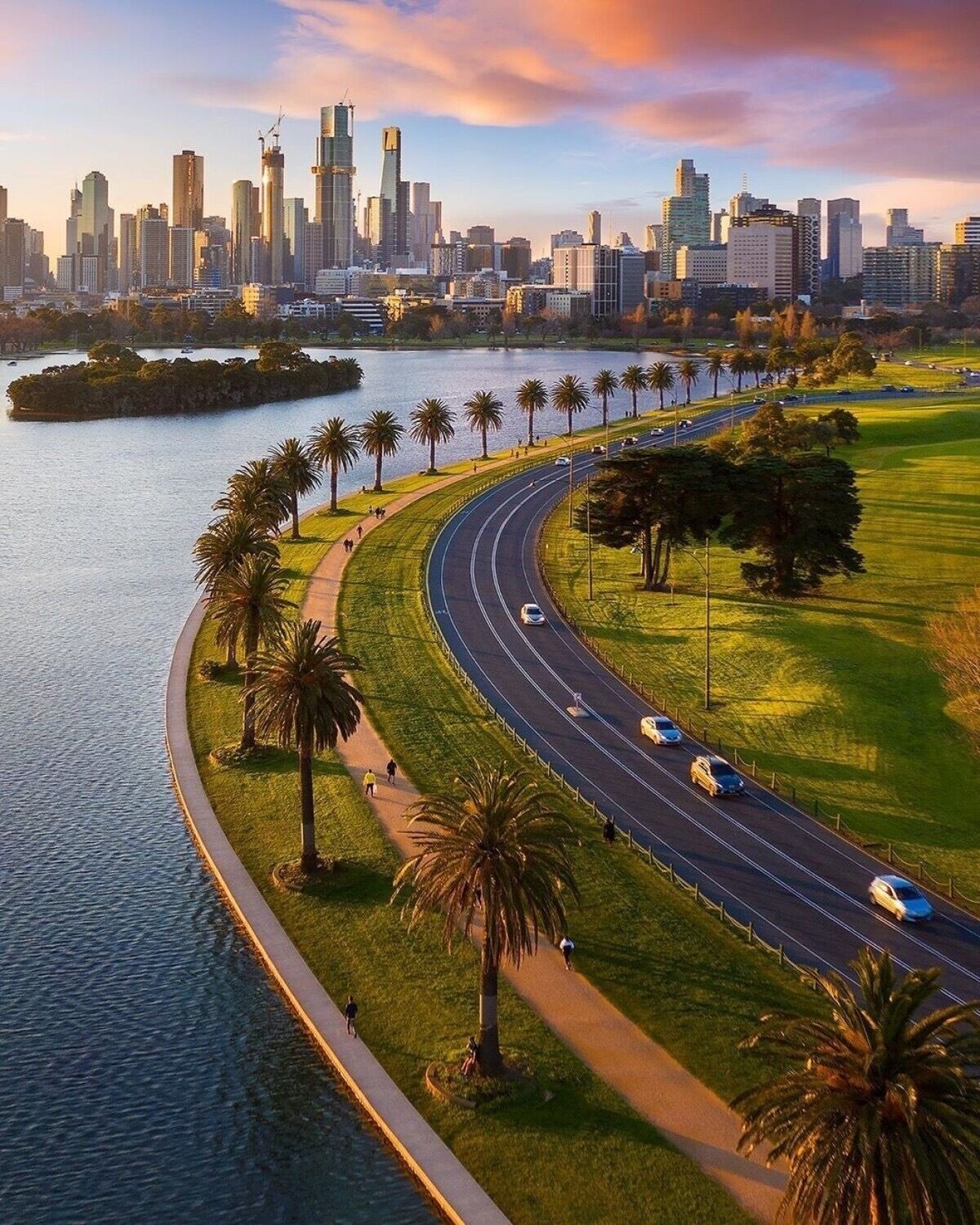 A city skyline with modern buildings, a curved road, and a waterfront with palm trees.