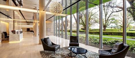 A modern lobby with a reception desk, leather seating, a patterned rug, and large windows offering a view of the outdoors.
