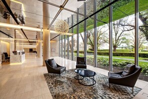 Un hall d’entrée moderne doté d’un comptoir de réception, de fauteuils en cuir, d’un tapis à motifs et de grandes fenêtres offrant une vue sur l’extérieur.