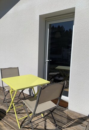 Eine Terrasse mit einem gelben Tisch und zwei Stühlen, einer Glastür und einer weißen Wand mit Struktur.