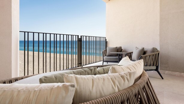 A balcony with a view of the beach, a wicker sofa with cushions, and a small table. - Grand Hyatt Los Cabos Resort, Golf & Spa, All-Inclusive (Cabo San Lucas)