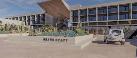 A Grand Hyatt hotel with a modern design, featuring a large parking area and a distinctive architectural structure with a slanted roof.