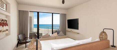 A hotel room with a bed, a TV, a ceiling fan, a view of the beach, and a seating area with a table and chairs.