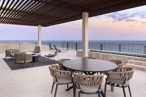 A covered outdoor seating area with a view of the ocean, featuring a round table and wicker chairs.