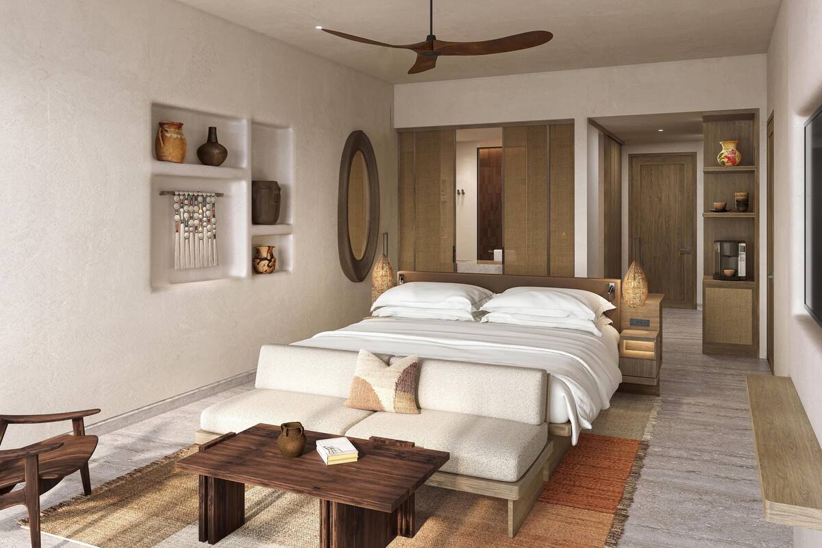 Une chambre moderne avec un grand lit, un ventilateur de plafond, un canapé, une table basse et une salle de bain visible à travers une porte coulissante.