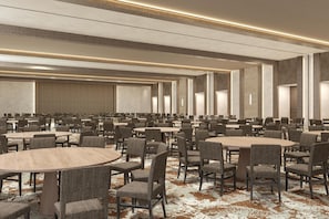 Une grande salle de conférence dotée de nombreuses tables rondes et de chaises, de hauts plafonds et d’un sol recouvert de moquette.