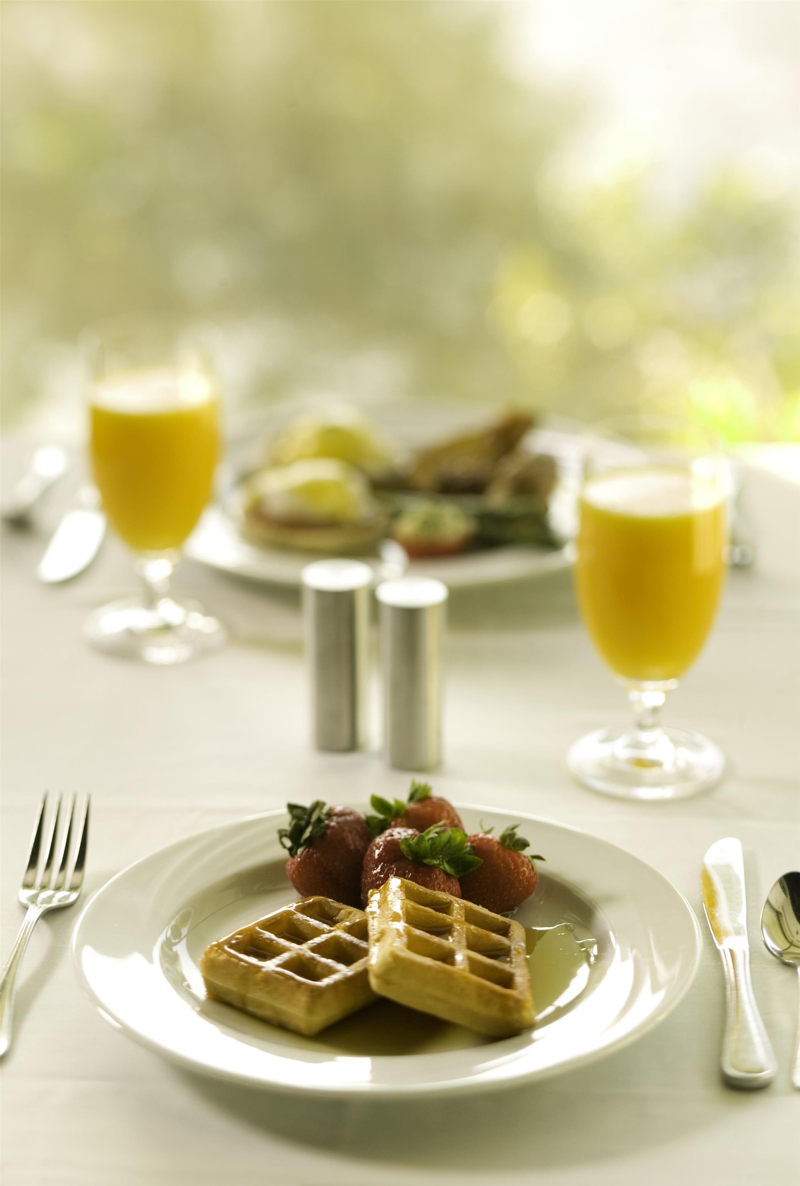Une table dressée pour le petit-déjeuner, avec des gaufres, des fraises et deux verres de jus d’orange.