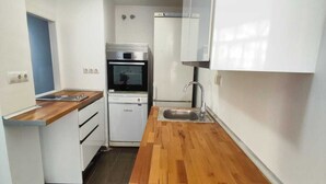 Een kleine keuken met een houten aanrecht, een inbouwoven en witte kastjes.