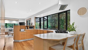A modern kitchen with a large island, wooden cabinets, and a view of greenery outside. - Luxury Coastal Escape at Kingston Beach (Kingston Beach)