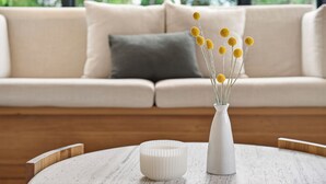 A white vase with yellow flowers on a round table, a white bowl, and a beige sofa with a gray pillow in the background. - Luxury Coastal Escape at Kingston Beach (Kingston Beach)