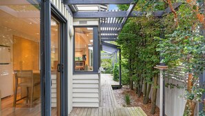 A wooden deck with a glass door leading to a room, a pergola, and a garden with a wooden fence. - Luxury Coastal Escape at Kingston Beach (Kingston Beach)