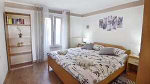 A bedroom with a bed, a bookshelf, a window with curtains, a bedside table, and wall art. - Bright flat with sea view terrace (Umag)