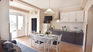 A modern kitchen with white cabinets, a dining table set for four, and a sofa in the living area. - Bright flat with sea view terrace (Umag)