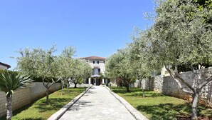 A stone pathway leading to a building with a tiled roof, surrounded by trees and a stone wall. - Bright flat with sea view terrace (Umag)
