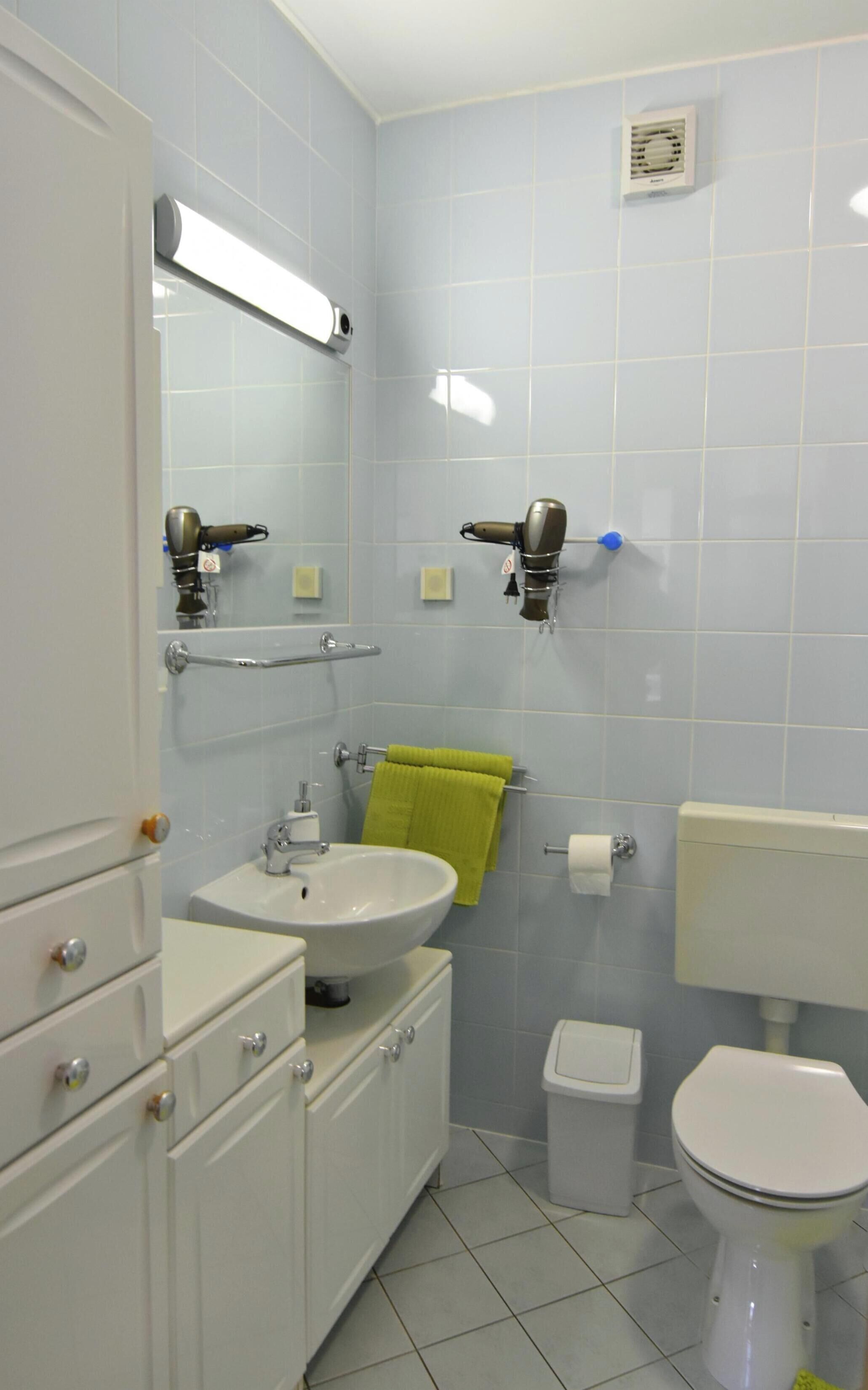 Een badkamer met een wit wastafelmeubel, spiegel, handdoekhouder, toilet en een vuilnisbak.