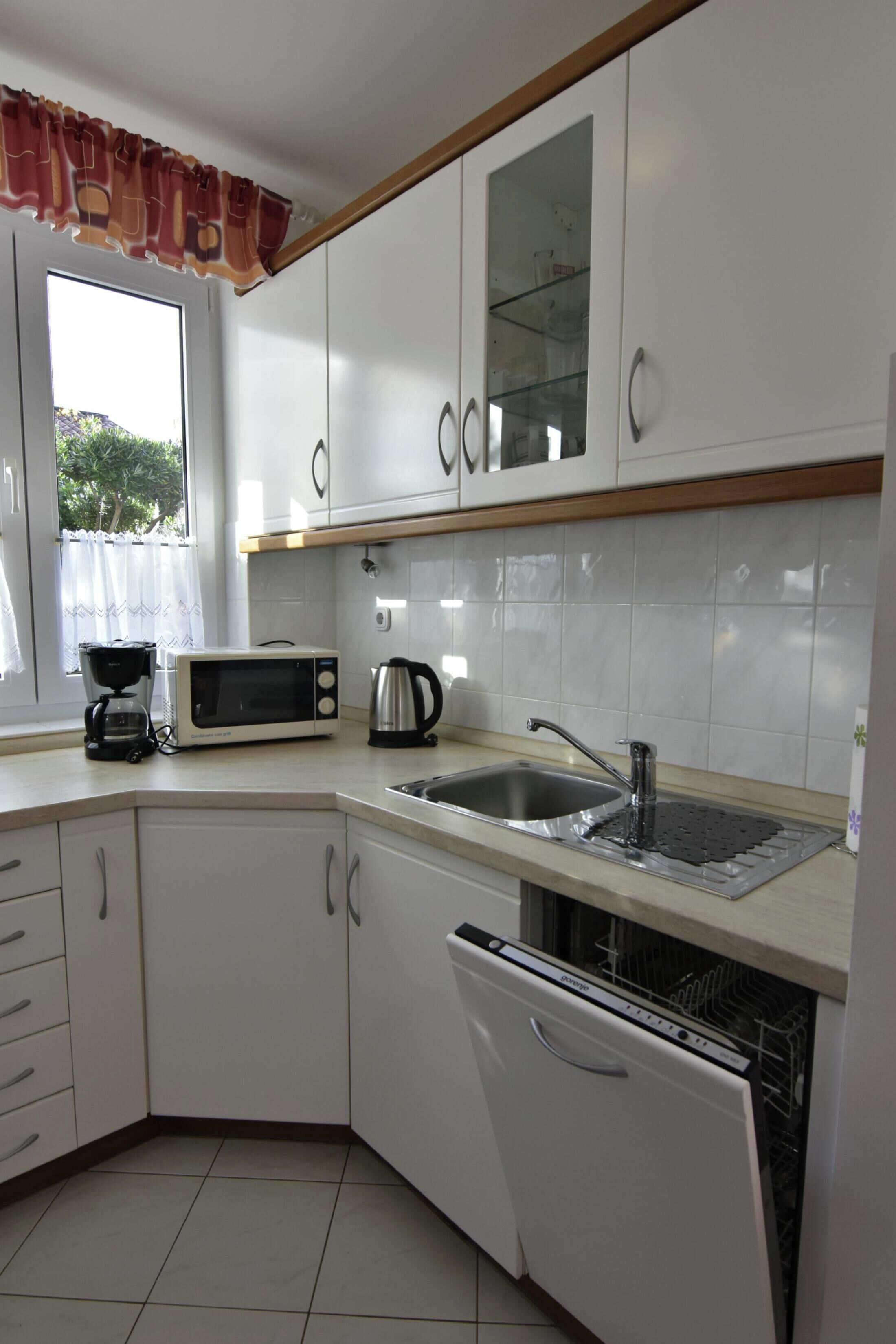 A kitchen with white cabinets, a microwave, a coffee maker, a sink, and a dishwasher.
