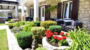 Un bâtiment en pierre doté d’un patio couvert, d’un espace extérieur aménagé pour s’asseoir et d’un jardin orné de fleurs rouges.
