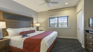 Habitación de hotel con cama, mesitas de noche, ventilador de techo, ventana con persianas y televisor.