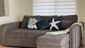 Un canapé d’angle gris, accompagné d’un pouf assorti, de deux coussins décoratifs et d’un plaid.