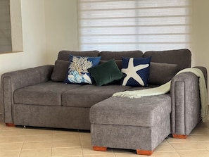 A grey sectional sofa with a matching ottoman, two decorative pillows, and a throw blanket.