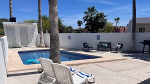 Une piscine avec des chaises longues, un barbecue et des palmiers.