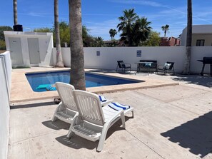 A swimming pool with lounge chairs, a barbecue grill, and palm trees.
