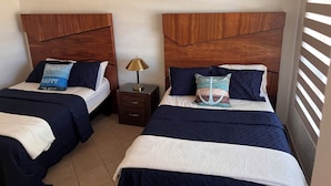 Deux lits avec des têtes de lit en bois, une table de chevet avec une lampe et un appareil de climatisation fixé au mur.