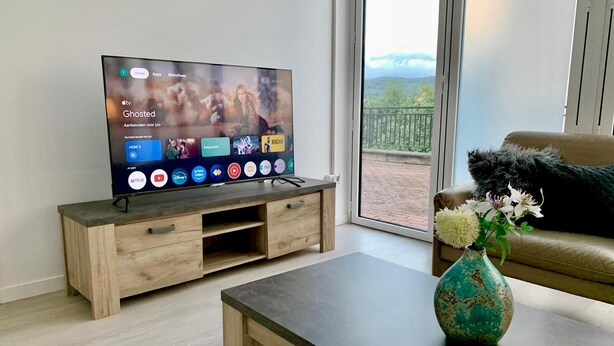 Moderni olohuone, jossa on litteänäyttöinen televisio, puinen mediakeskus, sohvapöytä ja näkymä parvekkeelle, jossa on kaide.