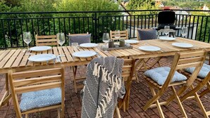 Un espace de restauration en plein air offrant une vue sur un paysage vallonné, avec un barbecue et une table dressée pour quatre personnes.