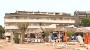 Ein Hotel mit mehreren Balkonen, Sitzgelegenheiten im Freien mit Sonnenschirmen und einem Sandstrand.