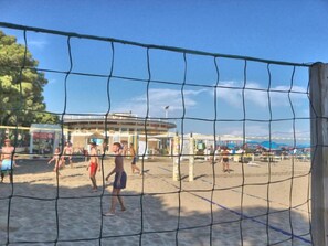 A beach volleyball court with a net, sand, and a building in the background. - Renovated residence near the sea (Lignano Sabbiadoro)