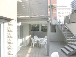 A covered outdoor patio with a table and chairs, a staircase, and a stone wall. - Modern residence just steps from the beach (Lignano Sabbiadoro)