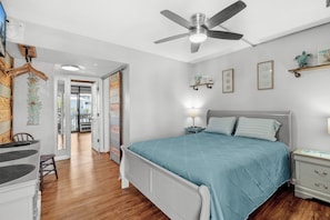 A bedroom with a bed, bedside table, nightstand, ceiling fan, and a view into the adjacent room. - Ocean View Getaway with Pool & Beach Access (Myrtle Beach)