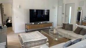 Een moderne woonkamer met een flatscreen-televisie, een glazen salontafel, een bank en een bed met een beddeken met dessin.