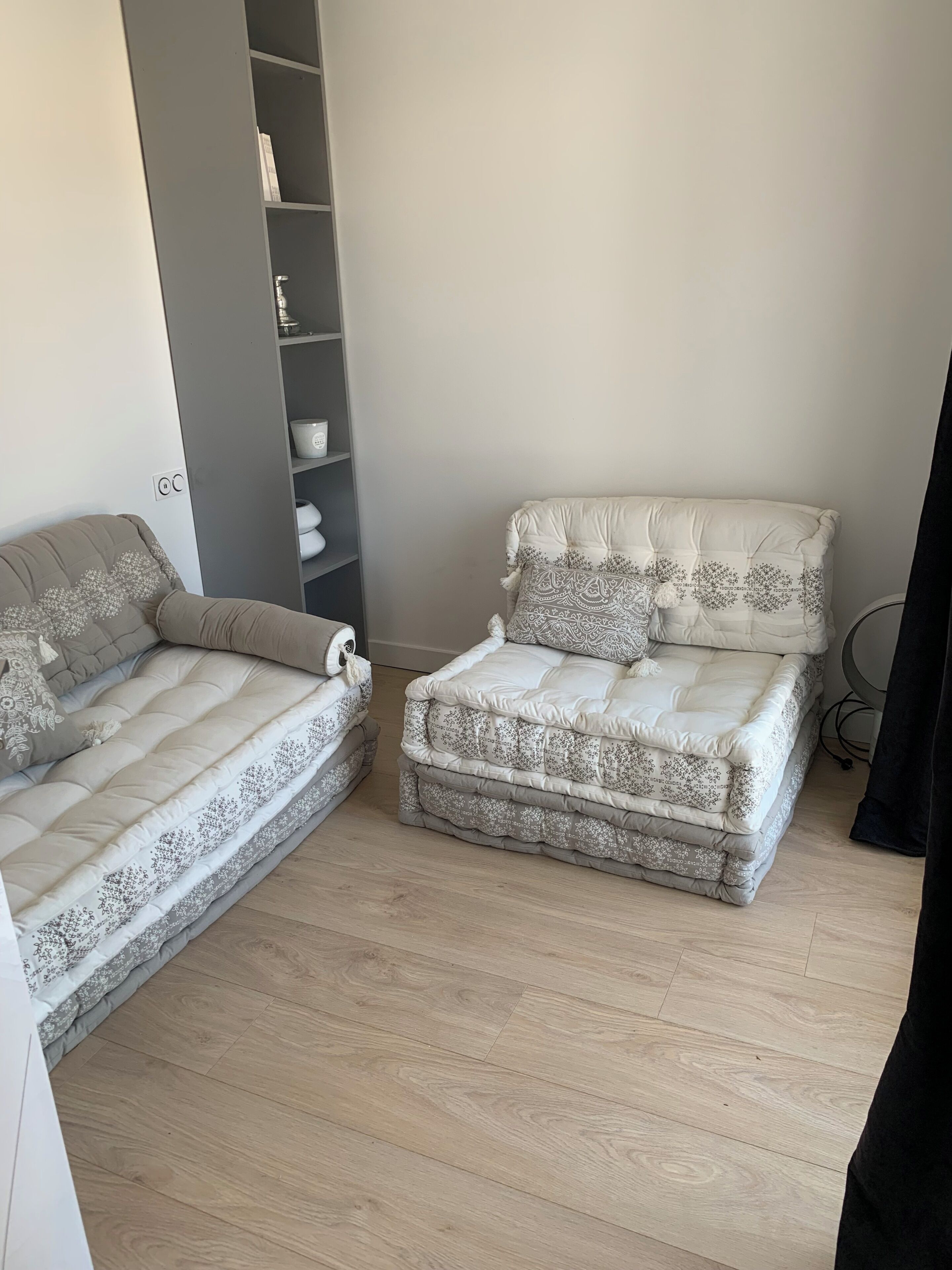 A bedroom with two beds, a grey wardrobe, and a bedside table.