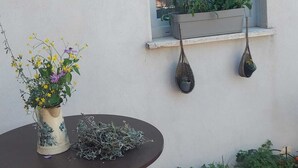 Ein Fenster mit weißem Rahmen, ein Blumentopf auf dem Sims und ein Tisch mit einer Blumenvase und einem Korb mit Grünpflanzen.