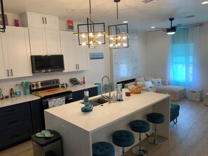 Una cocina moderna con armarios blancos, una isla central con taburetes y un microondas, además de un ventilador de techo.