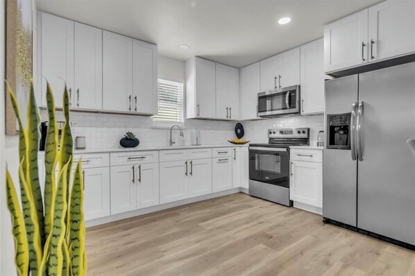 Una cocina moderna con armarios blancos, electrodomésticos de acero inoxidable y piso de madera.