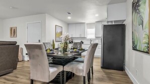 A modern kitchen with white cabinets, a black refrigerator, and a dining area with a table set for four. - Cozy Retreat on Dana Drive (Haltom City)