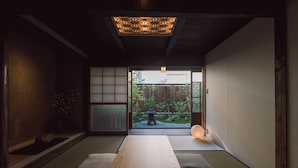 A traditional Japanese room with tatami flooring, a low table, sliding doors, and a view of a garden.