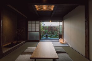 Une pièce de style japonais traditionnel, avec un sol recouvert de tatamis, une table basse, des portes coulissantes et une vue sur un jardin.