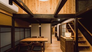 A wooden interior with a dining table and chairs, a staircase, and a lamp.