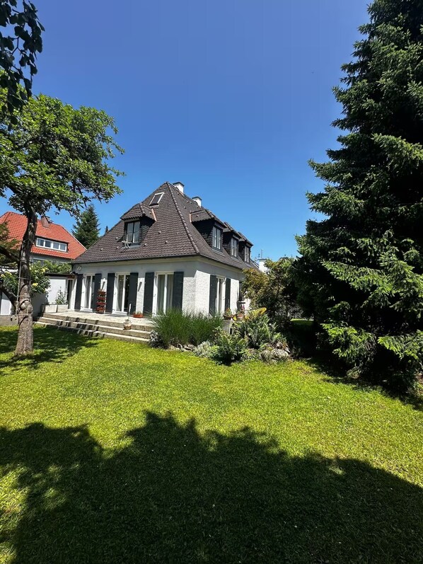Une maison à deux étages avec un toit en pente, un porche à l’avant avec des marches et une pelouse bien entretenue.