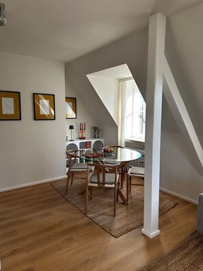 Un coin repas comprenant une table ronde en verre, des chaises en bois, un tapis tissé et des œuvres d’art encadrées accrochées aux murs.