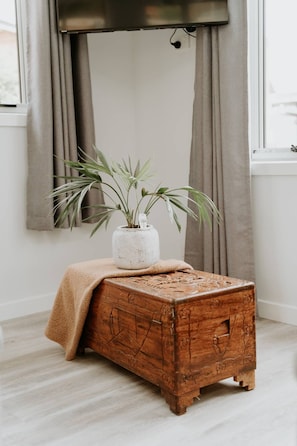A wooden chest with carvings, a potted plant, and a beige throw blanket on a light-colored floor.