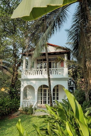 Um edifício de dois andares com varanda, cercado por vegetação exuberante e palmeiras.