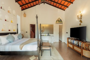Quarto com cama, mesa de cabeceira e televisão sobre um suporte de madeira.